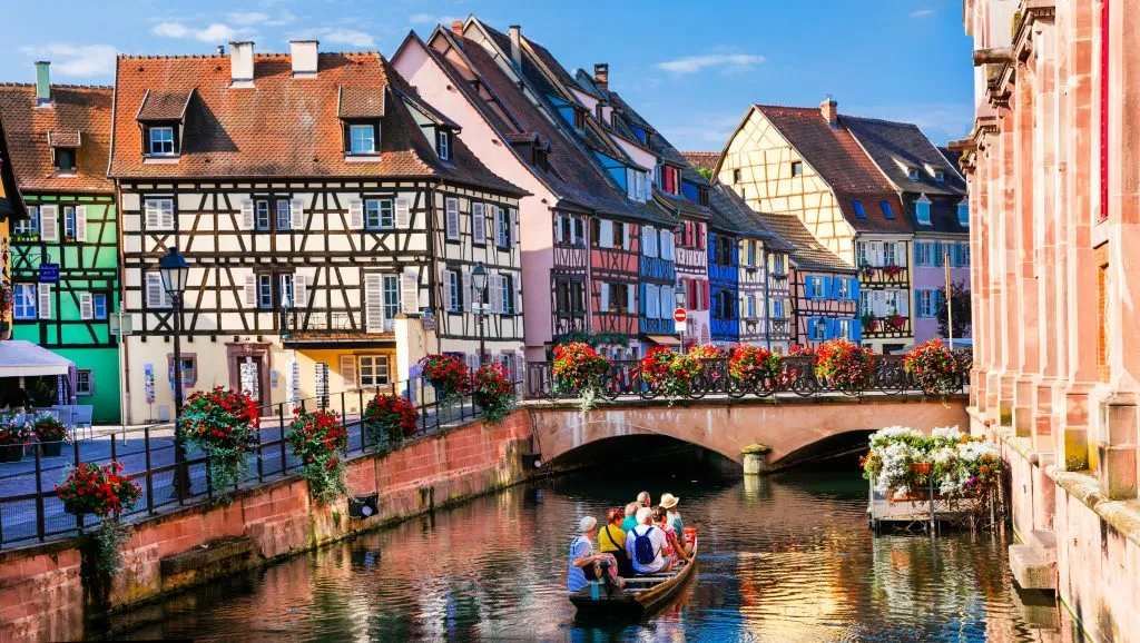 canal in colmar france with small boat with tourists in it, buildings in the background