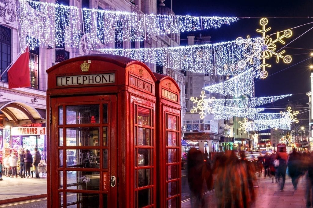 Classic red telephone booths in London with Christmas lights hanging above them and shoppers walking by