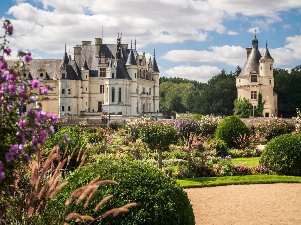 Château Chenonceau as seen from across the garden with pink flowers in the foreground. Château Chenonceau is one of the best day trips from paris france