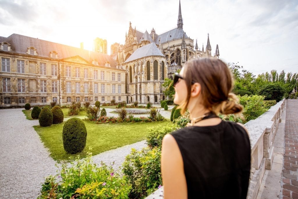 Young woman in a black tank top and sunglasses standing in front of the Reims cathedral