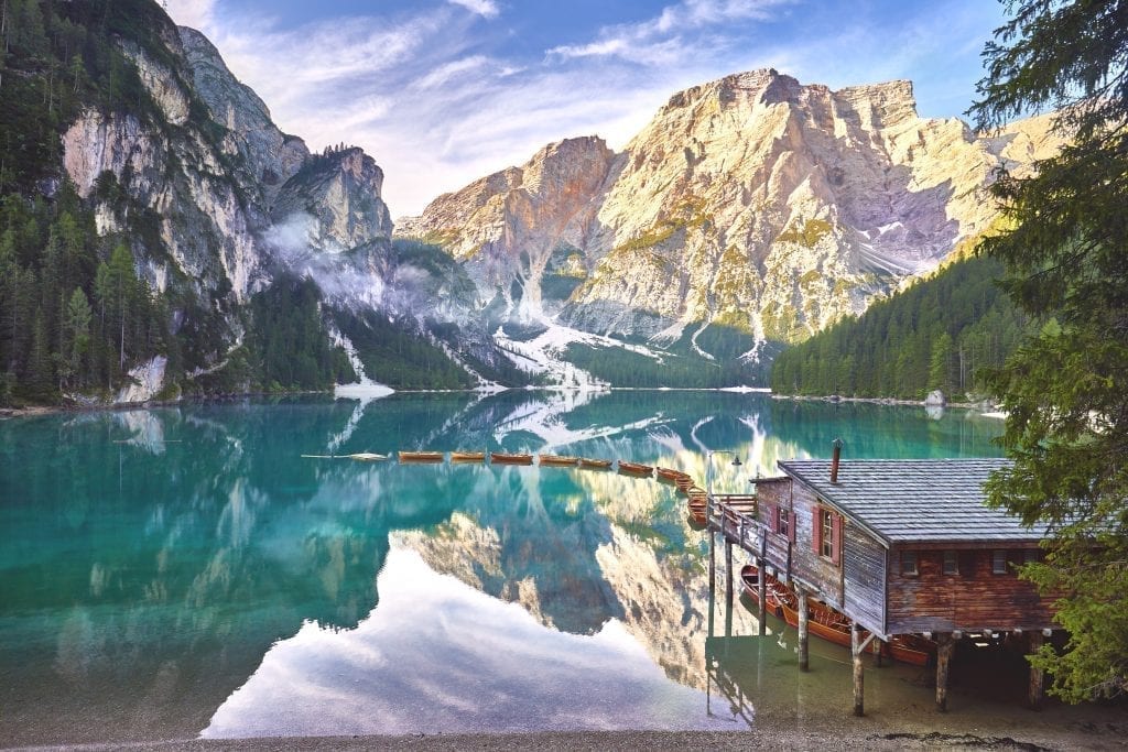 Lago di Braies in the early morning with a line of boats tied to the dock at the boathouse. Lago di braies is at the top of any list of italy beautiful places