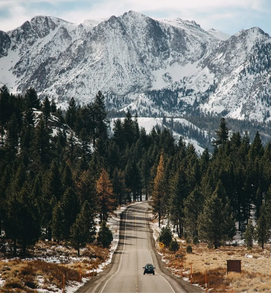 lone car driving on the june lake loop with the mountains in the background of the photo