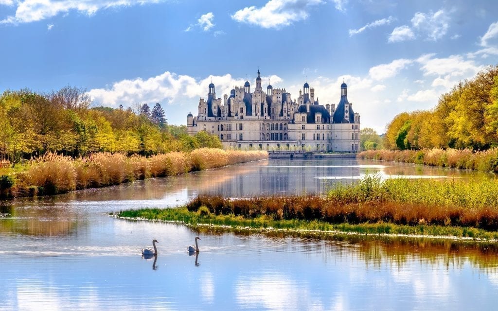 Château de Chambord as seen from a distance with a pond in the foreground that has 2 swans on it