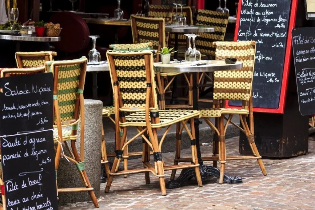 Sidewalk table at a small restaurant in Paris with 2 chairs visible and menu boards to the side