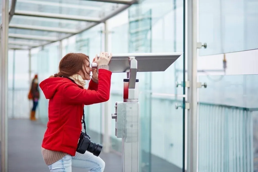 Woman in a red jacket looking through a viewing device on Montparnasse Tower Paris France