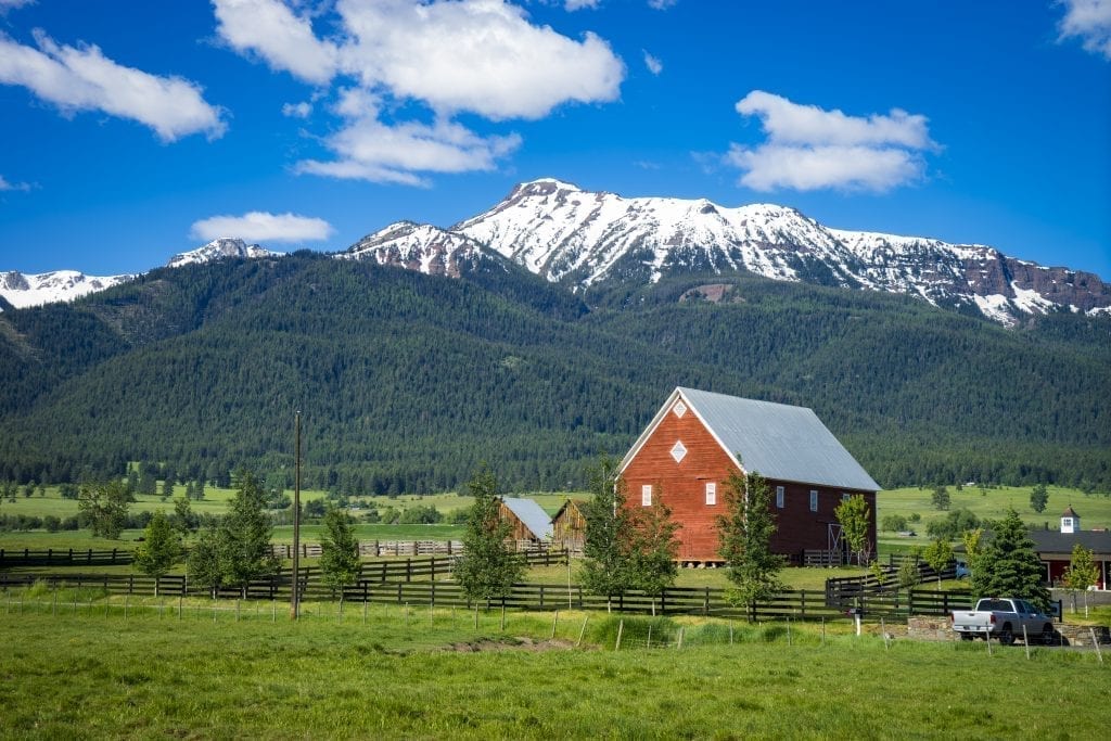 Wallowa mountains in northeastern Oregon with a red barn in the foreground. northeast oregon is an offbeat usa west coast road trip itinerary