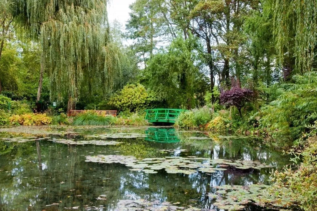 Water gardens of Giverny with green bridge visible in the center back. Giverny is one of the most fun day trips from Paris France