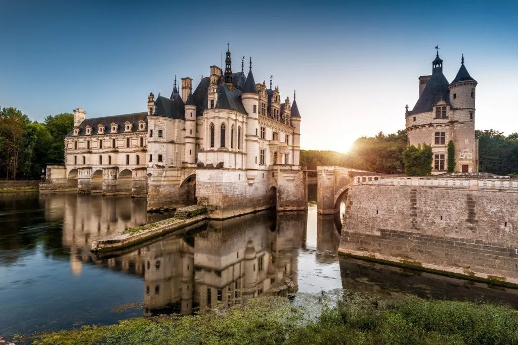 Château Chenonceau as seen from the side at sunset with water in the foreground. This chateau is one of the best day trips from Paris France!