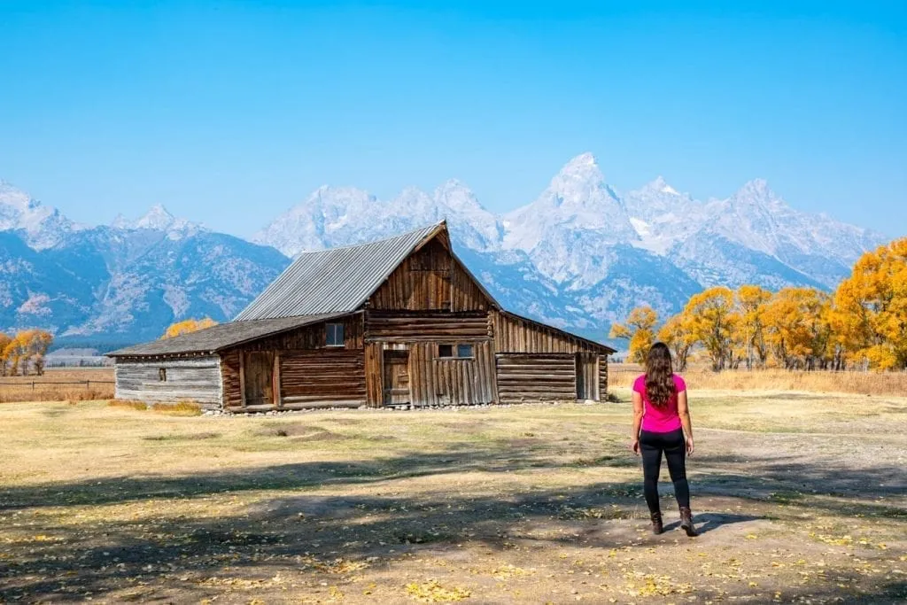 kate storm standing in front of a barn at mormon row in grand teton national park, a feature on many of the best usa road trip itineraries