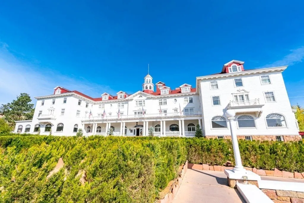 the front facade of the stanley hotel in estes park co with hedges visible in the foreground