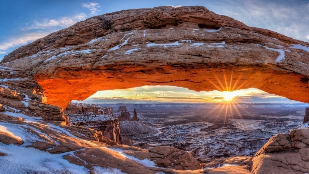 sunrise at mesa arch in canyonlands np with a sun flare and some snow on the ground