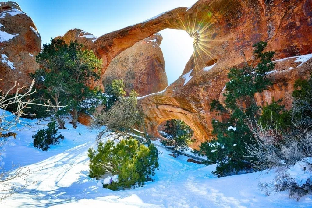 Arch in Arches NP with a sun flare and snow on the ground. arches in winter usa national parks to visit