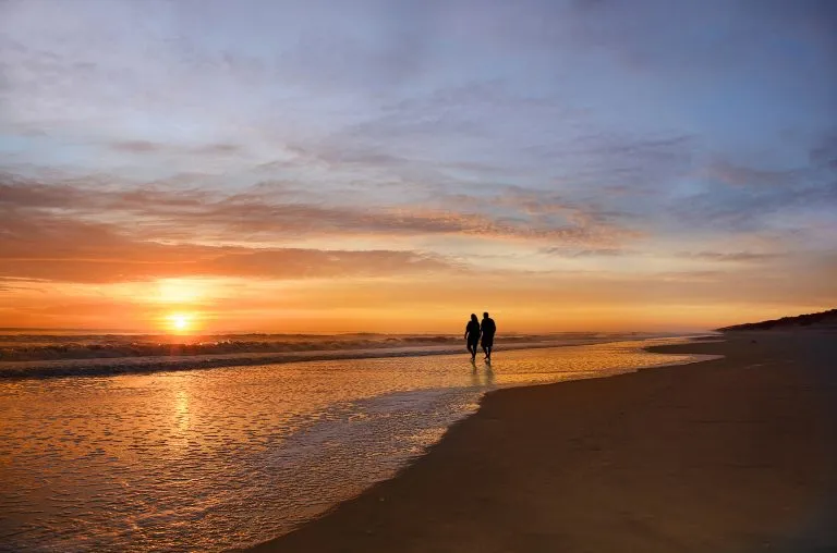 couple walking along the beach at sunset in the outer banks, one of the most romantic getaways in north carolina for couples