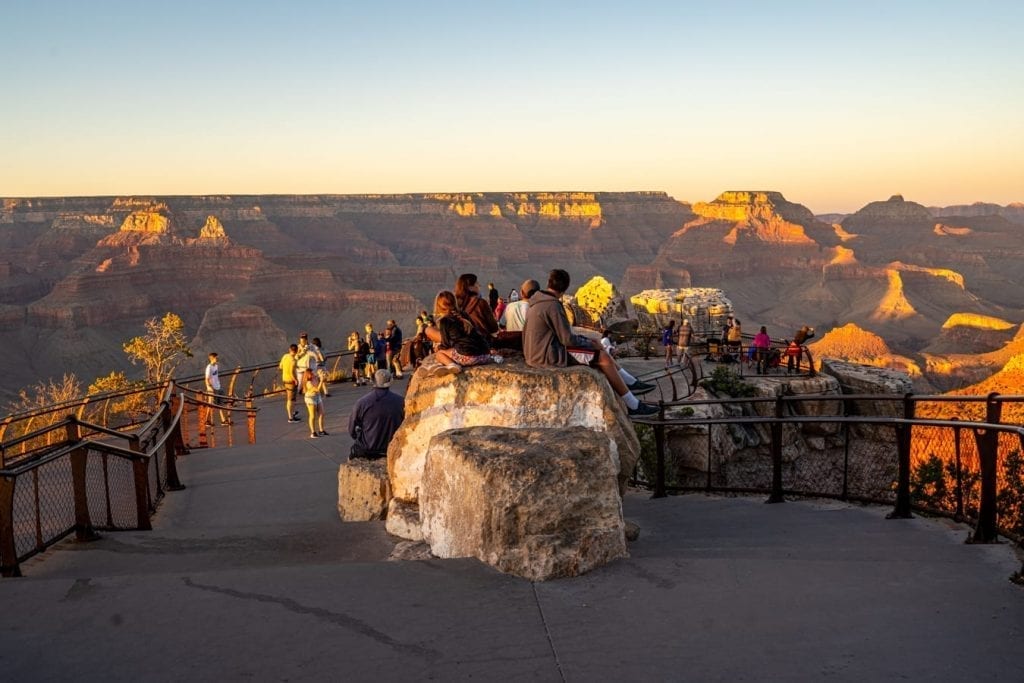 a crowd of people watching the sunset at mather point near grand canyon rim trail