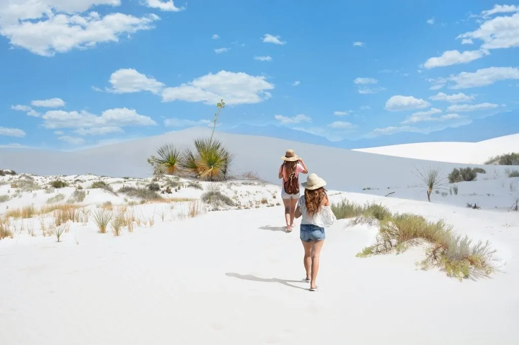 two young women hiking over sand dunes in white sands national park, one of the most beautiful national parks in america