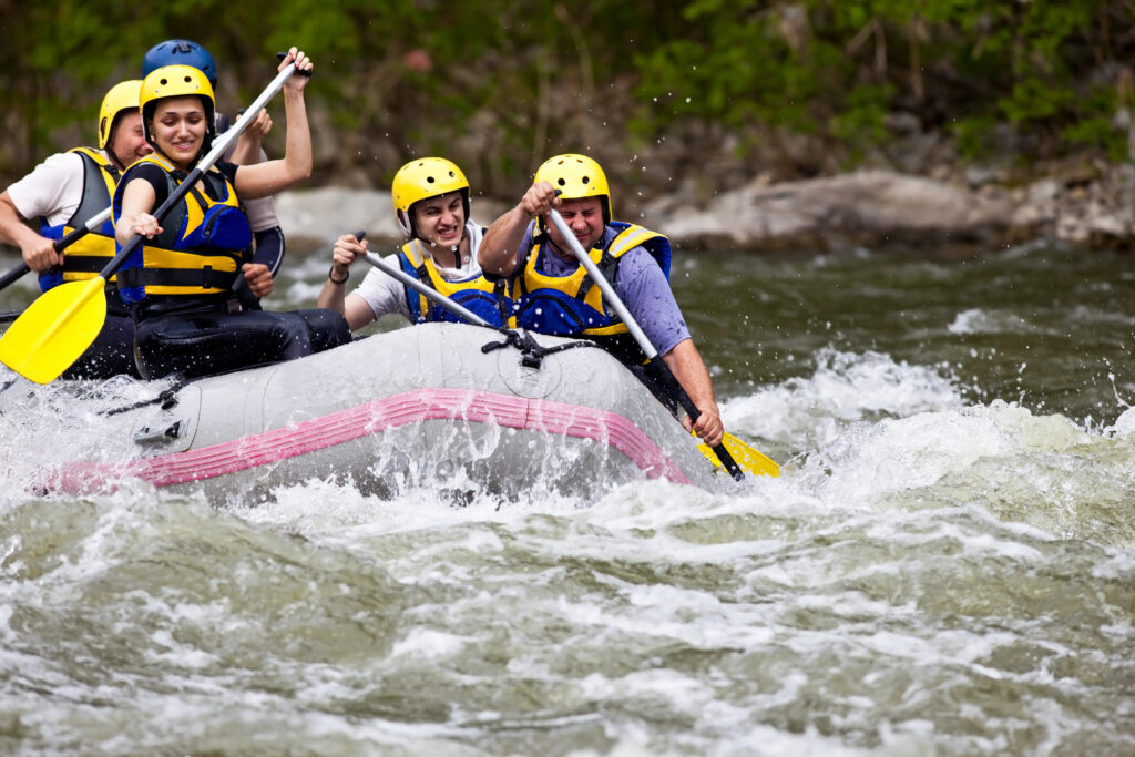 group of 5 people whitewater rafting on river with yellow helmets and paddles
