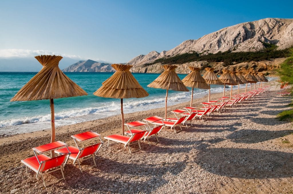 small beach on krk island with straw sunshades and red beach chairs