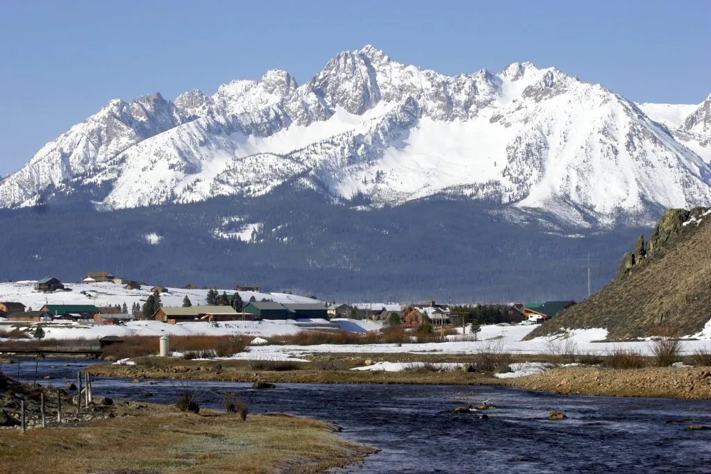 stanley idaho as seen from across a river, dwarfed by a snowcapped mountain in the background