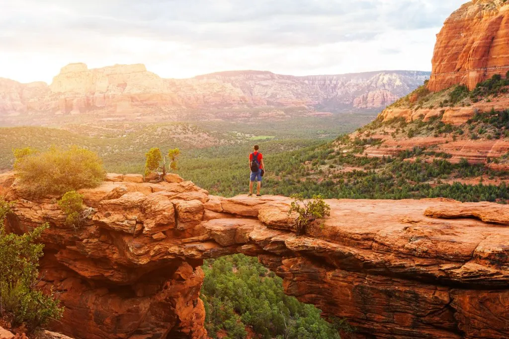 man in a red shirt standing on devils bridge in sedona arizona