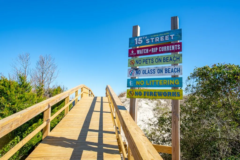 wooden boardwalk leading to the beach tybee island ga with colorful sign of rules to the right