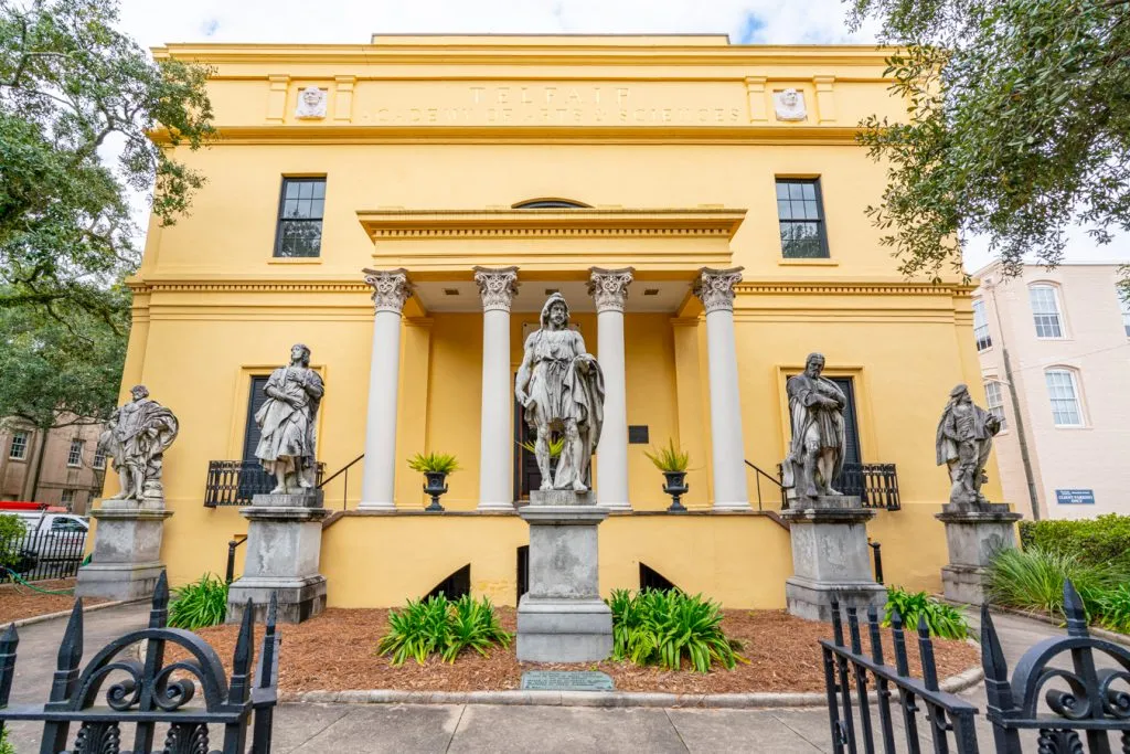 front facade of the telfair academy in savannah georgia, painted yellow with statues out front