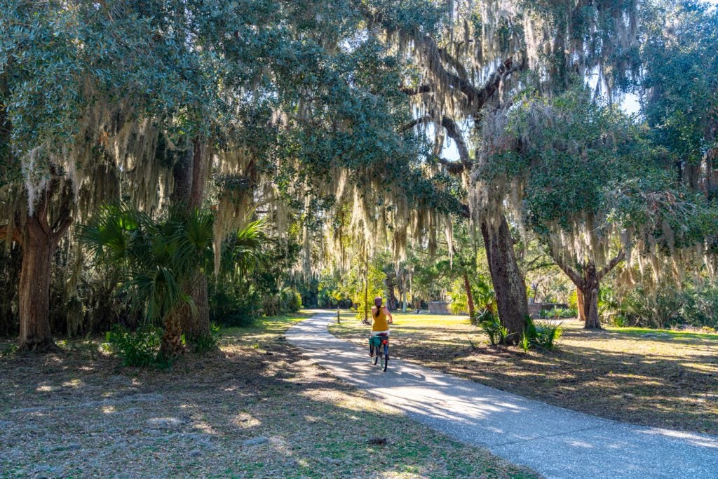 woman riding a bike through a path lined with spanish moss on jekyll island, one of the best day trips from savannah georgia