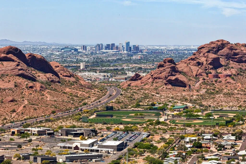 downtown phoenix arizona as seen from above, with red rock formations on either side of the photo that have a road cutting through them