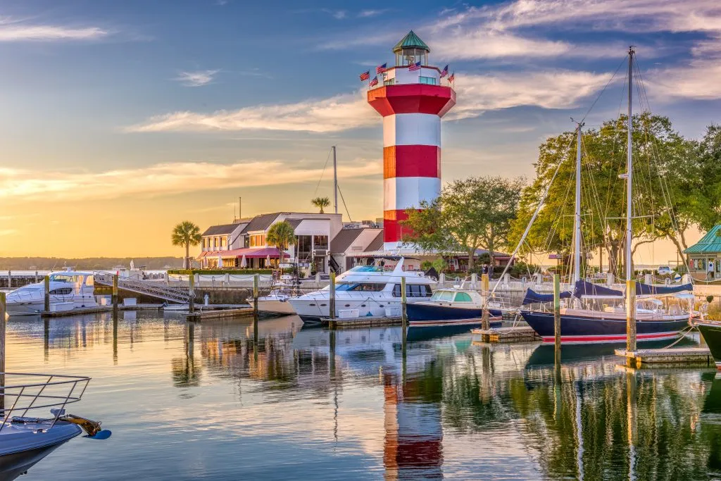 harbour town of hilton head island at sunset, with marina in the foreground and red and white striped lighthouse in the background