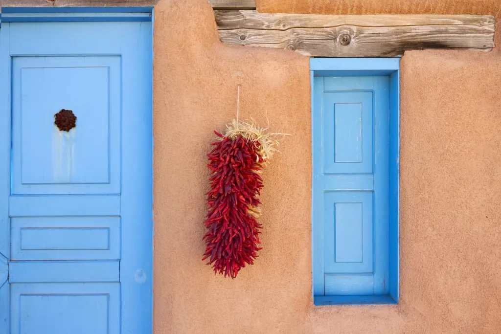 dried chiles hanging from an adobe building with a blue door in santa fe new mexico