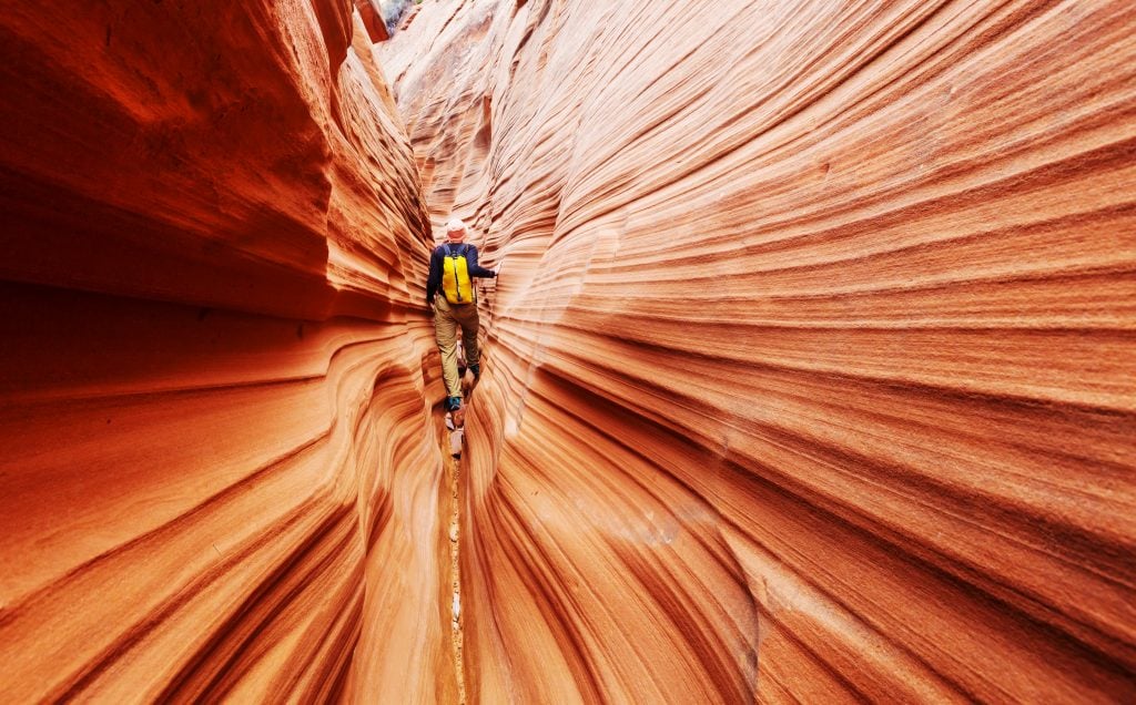 man in a yellow backpack hiking through zebra slot canyon, one of the best stops on a southwest road trip route