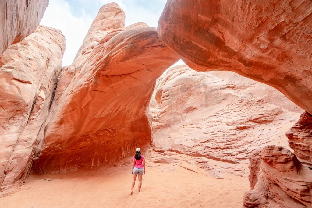 kate storm in a pink t-shirt standing underneath sand dunes arch, one of the best short hikes in arches np