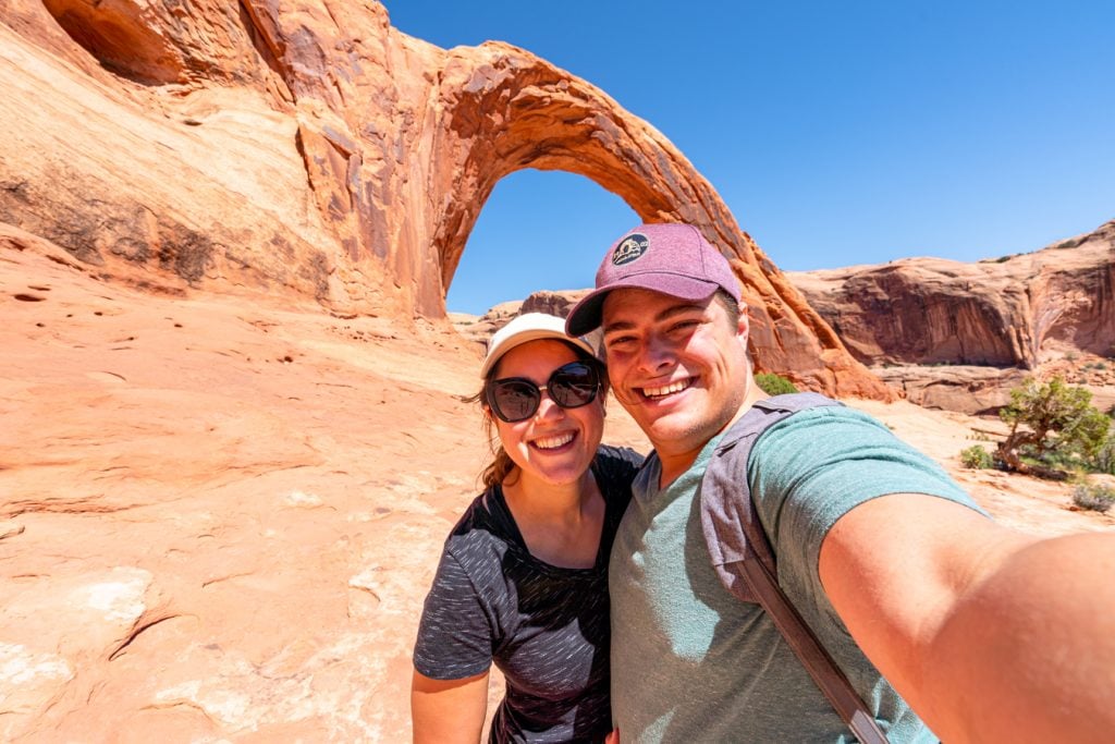 kate storm and jeremy storm taking a selfie in front of corona arch moab utah