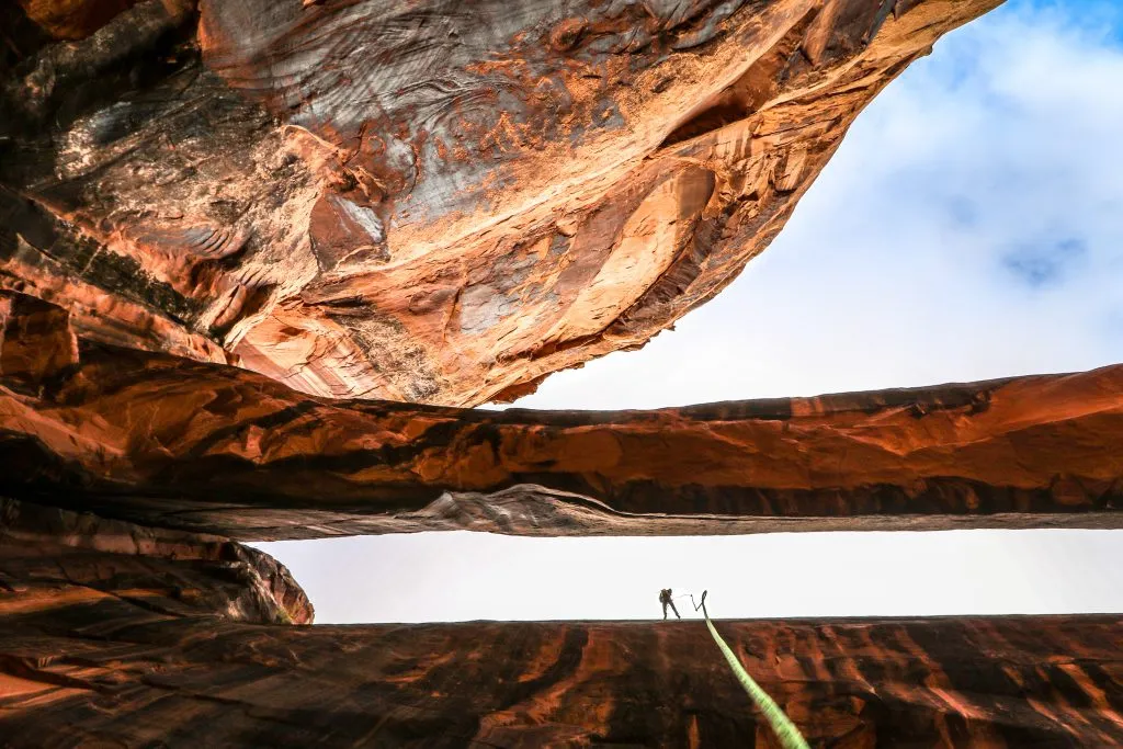 person preparing to rappell down a wall near moab, a green rope dangles in the foreground