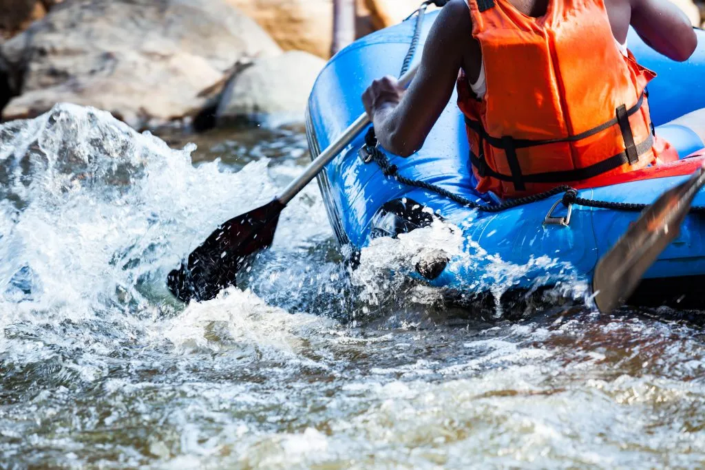 close up of a man paddling a blue white water raft through a rapid