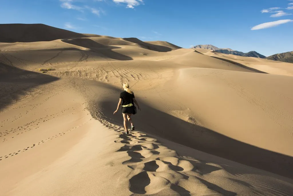 young woman hiking on a sand dune in great sand dunes national park, a bucket list colorado travel destinations