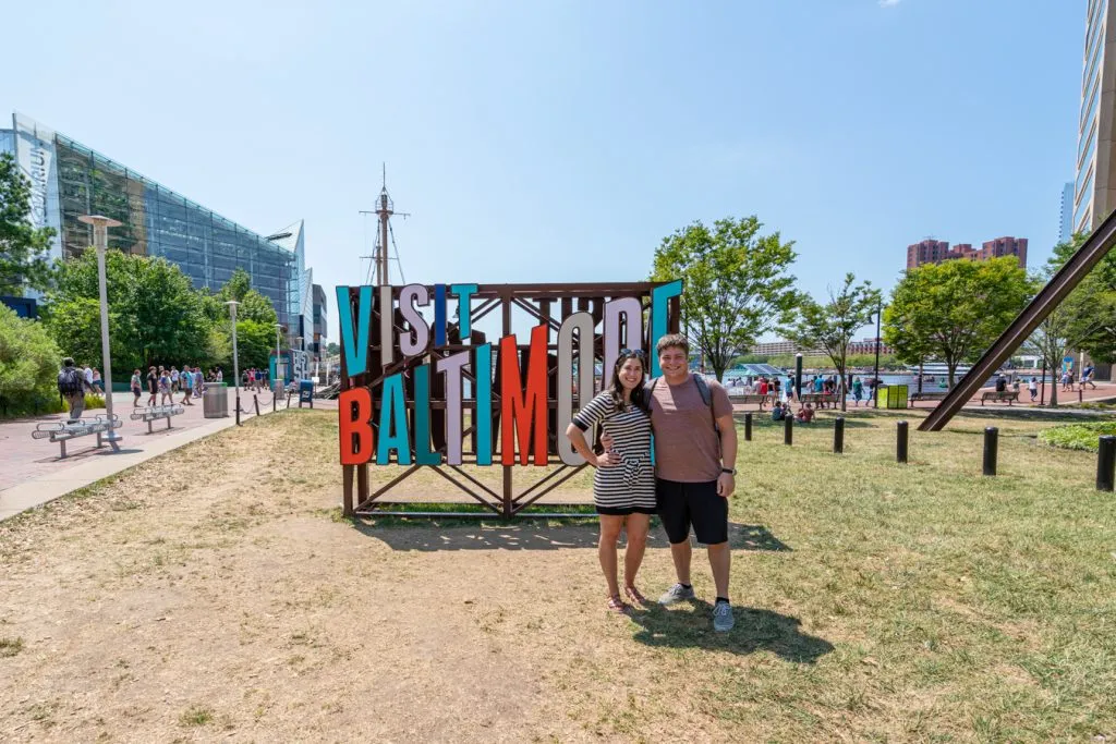 kate storm and jeremy storm posing with the colorful visit baltimore sign during a weekend getaway in baltimore md