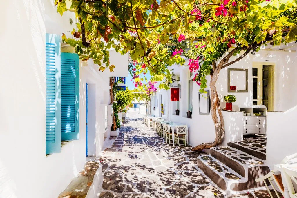 whitewashed buildings on a small street with pink flowers, a common sight when island hopping greece in 7 days