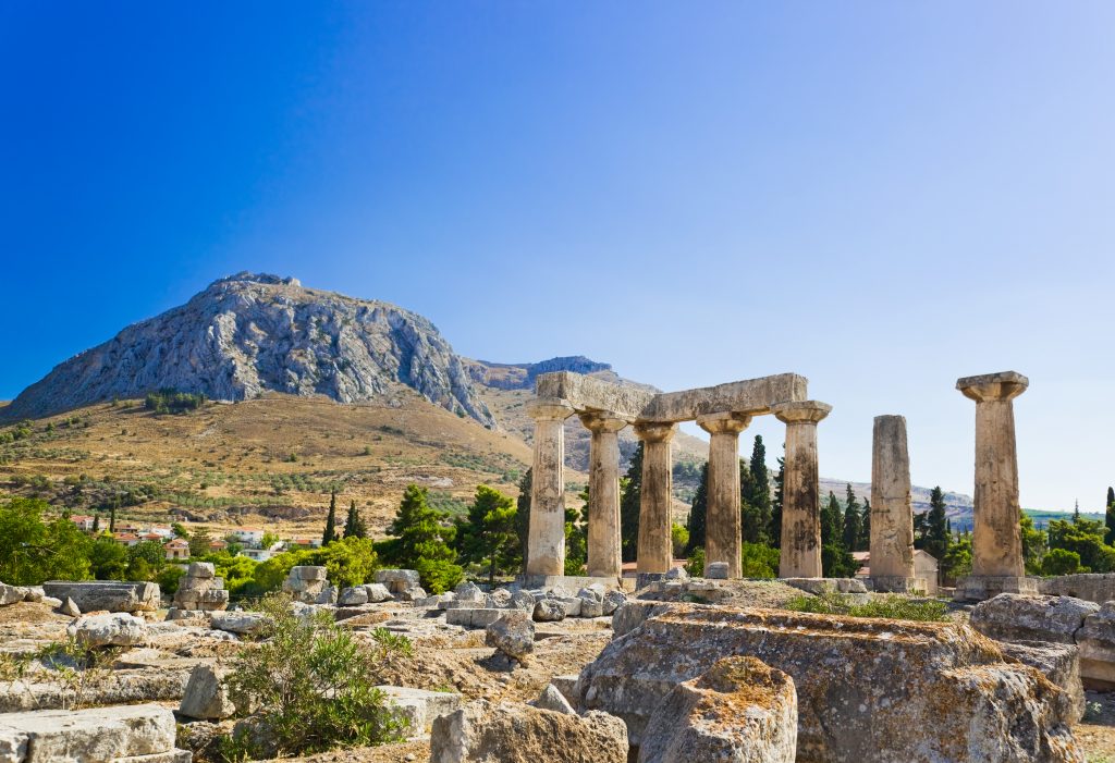 ruins of a temple in corinth greece with mountains in the background