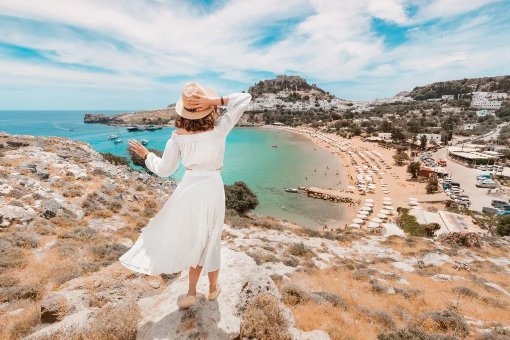 young woman in a white dress overlooking a beach in rhodes, a fun stop when exploring greece in 7 days island hopping