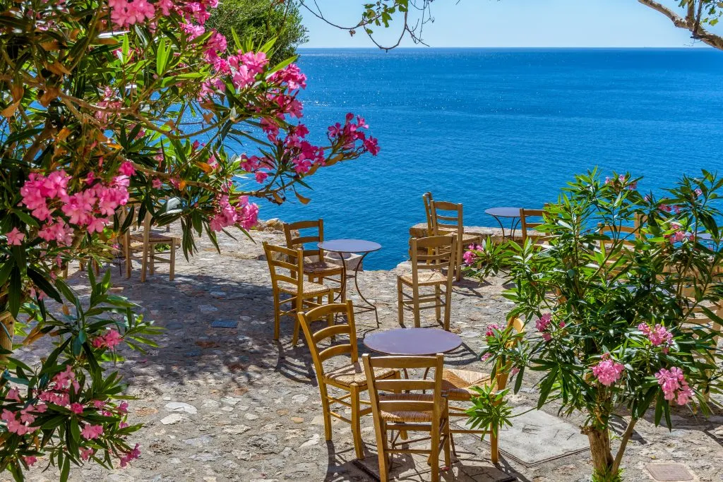 small tables overlooking the sea and surrounded by pink flowers as seen during an itinerary greece