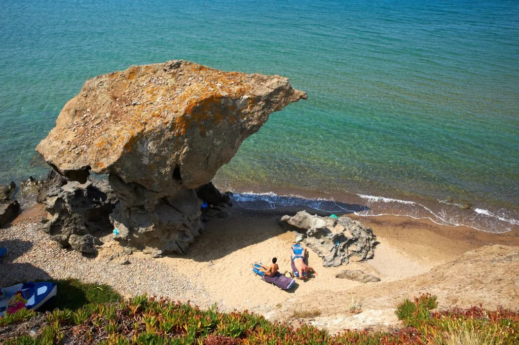 travelers sunbathing near a large boulder on the coast of lemnos greece