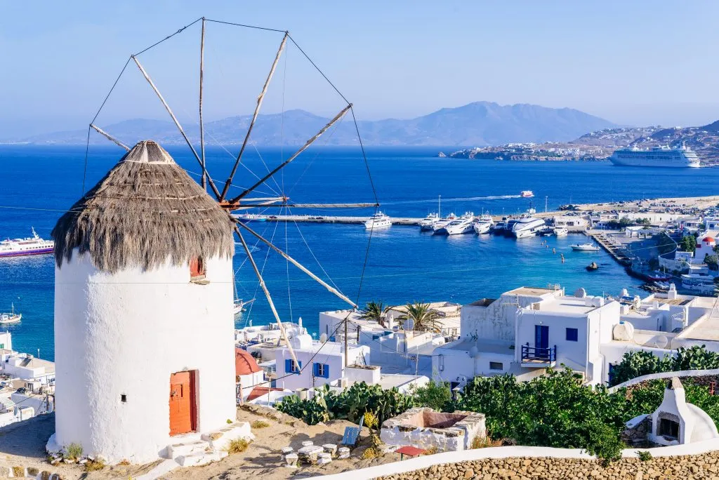 view of mykonos village and sea as seen from behind a windmill, which is prominent. mykonos is one of the most popular greek islands one week in greece