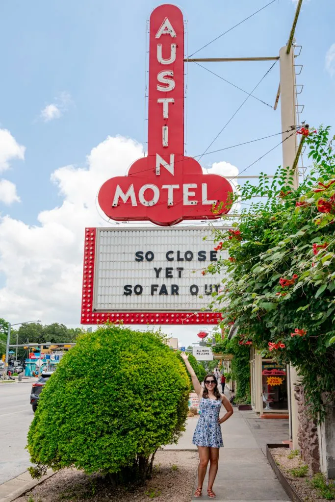 kate storm in a blue and white dress standing under the iconic austin motel sign in austin texas