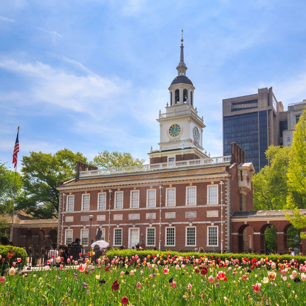 independence hall in philadelphia on a sunny day with red and pink flowers in the foreground. attractions in usa things to do