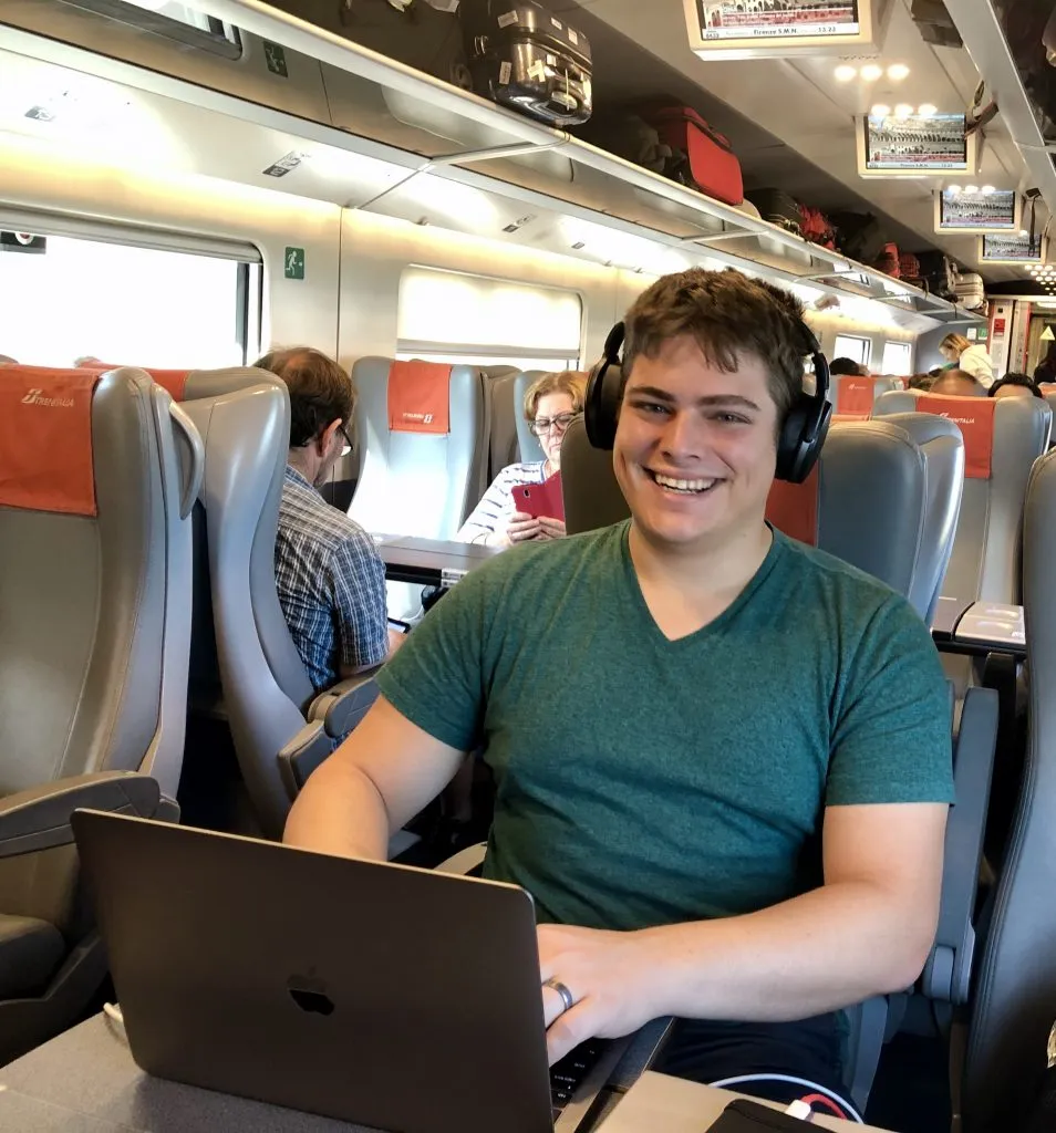 jeremy storm working on a macbook on a train in italy, combining work and traveling