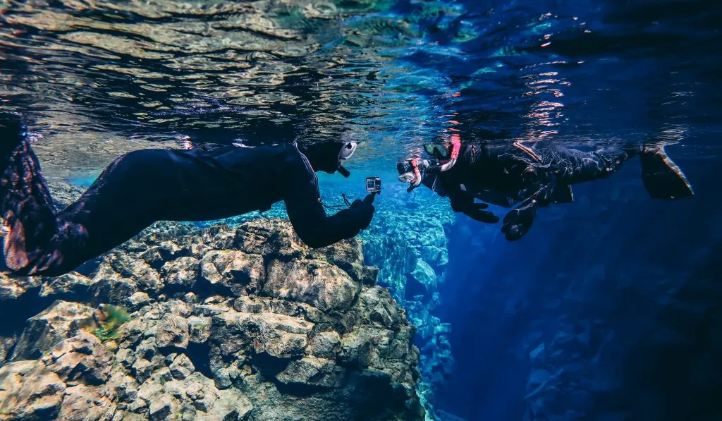2 people snorkeling in iceland, one is taking a photo of the other