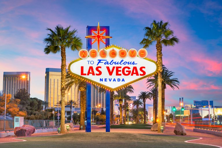 view of the famous welcome to las vegas sign framed by palm trees at sunrise, one of the best things to do in las vegas weekend getaway