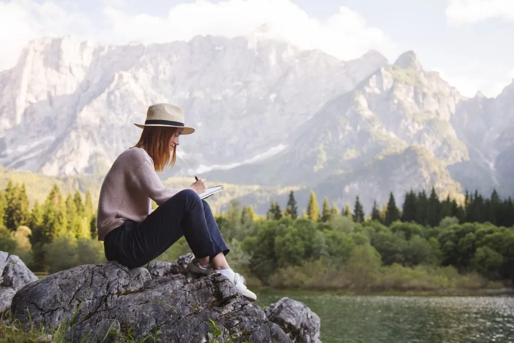 young woman writing travel writing prompts in the mountains