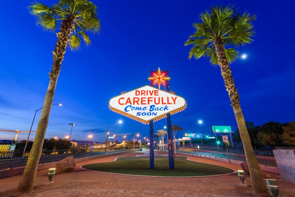 blue hour photo of las vegas sign reading "drive carefully" surrounded by palm trees, one of the best attractions las vegas 3 days