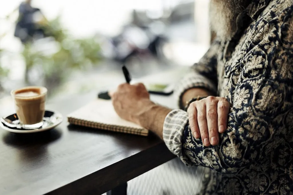 woman sitting in a cafe with coffee writing in a travel diary